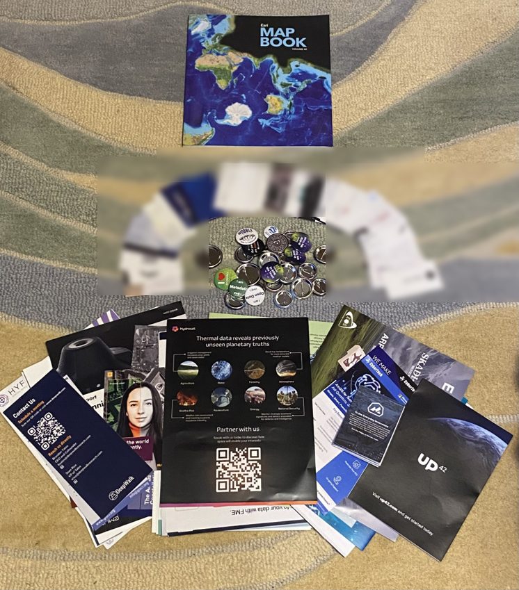 Esri Map Book, buttons, business cards, and flyers collected at the 2025 Esri User Conference